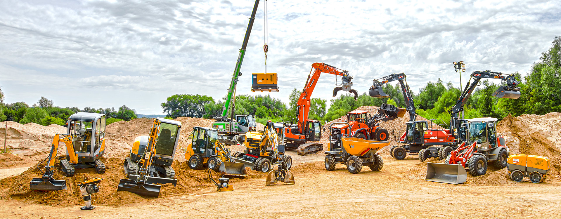 Arbeitswerkzeuge Eine Reihe von verschiedenen Baufahrzeugen und -geräten, darunter Bagger, Planierraupen, Lader, Kipper und ein Kran, sind auf einer unbefestigten Baustelle mit Sandhaufen und Bäumen im Hintergrund angeordnet.