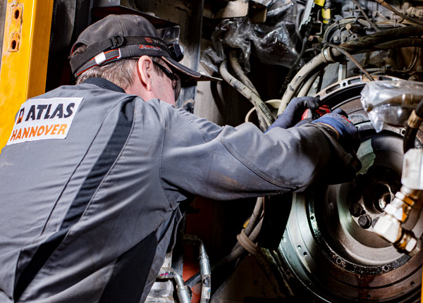 Ein Mechaniker, der Handschuhe und eine Mütze trägt, arbeitet an Maschinen und benutzt Werkzeuge, um einen großen Motor oder ein mechanisches Teil zu reparieren oder zu überprüfen.