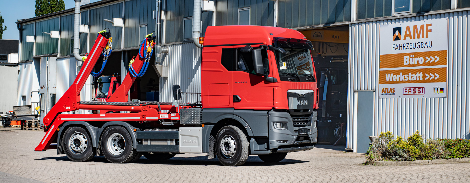 Fahrzeugbau für LKW Ein roter MAN-Lkw mit Absetzkipper steht vor dem Gebäude der AMF Fahrzeugbau, in der Nähe der Schilder, die auf die Eingänge Büro und Werkstatt hinweisen.